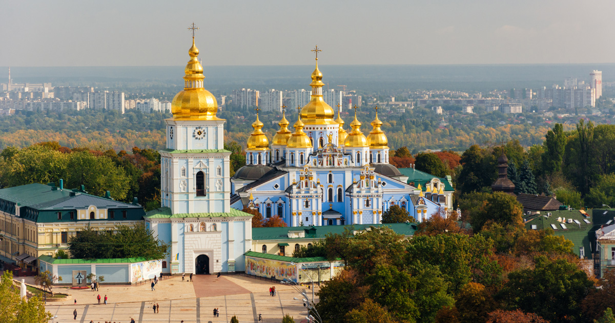 An Orthodox Church of Ukraine monastery is surrounded by trees with a city in the background. 